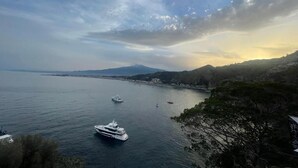 Vista costera con un yate, mar tranquilo y montañas a lo lejos.