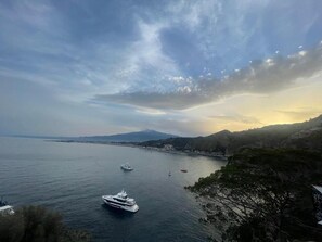A coastal view with a yacht, calm sea, and distant mountains.