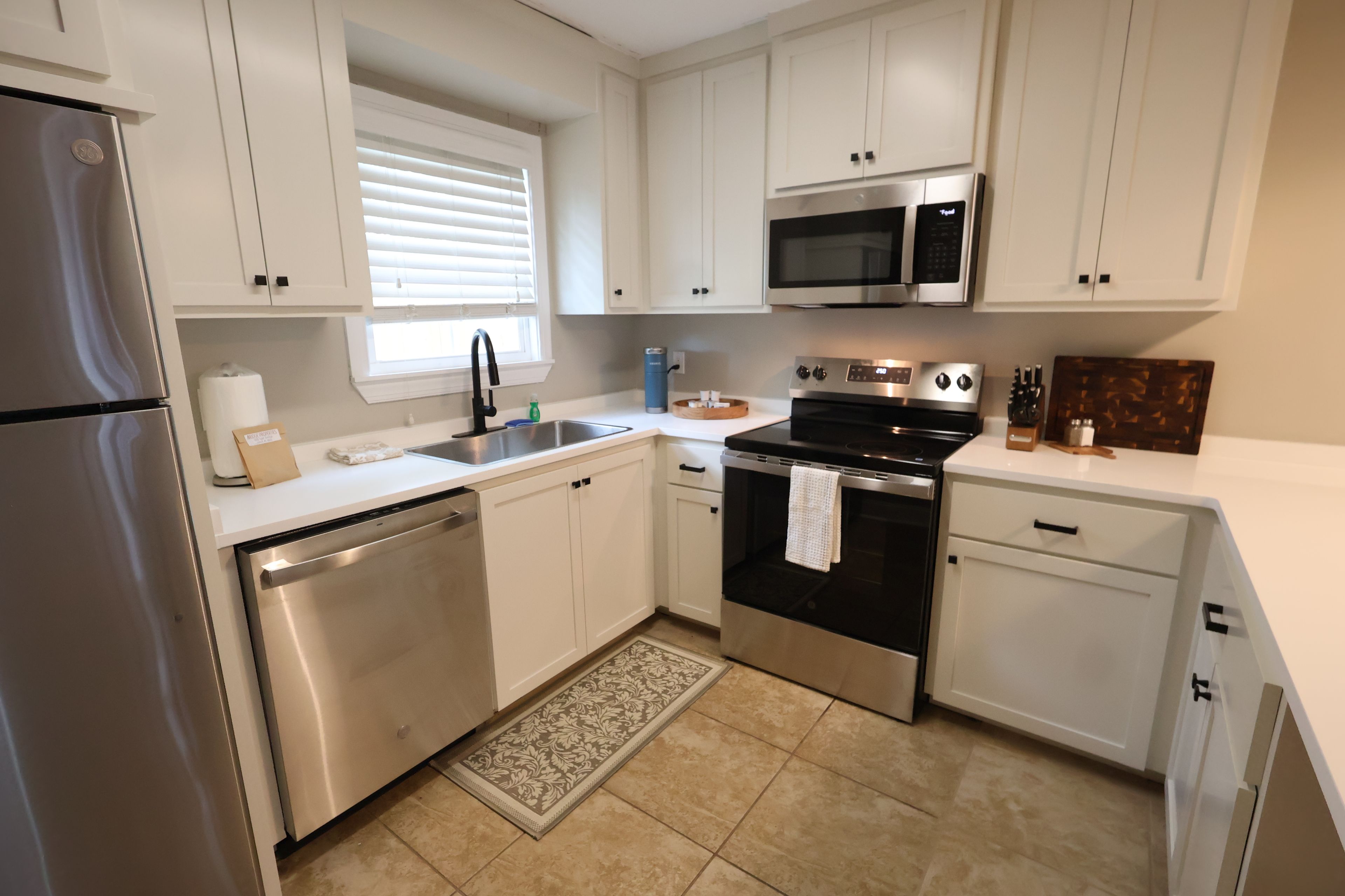 A modern kitchen with stainless steel appliances, white cabinetry, and a patterned rug.