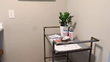 Un rincón de una habitación con un carrito metálico, una planta en maceta y una obra de arte enmarcada en la pared.