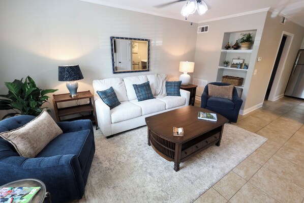 A living room with a white sofa, blue armchairs, a coffee table, and a small side table with a lamp.