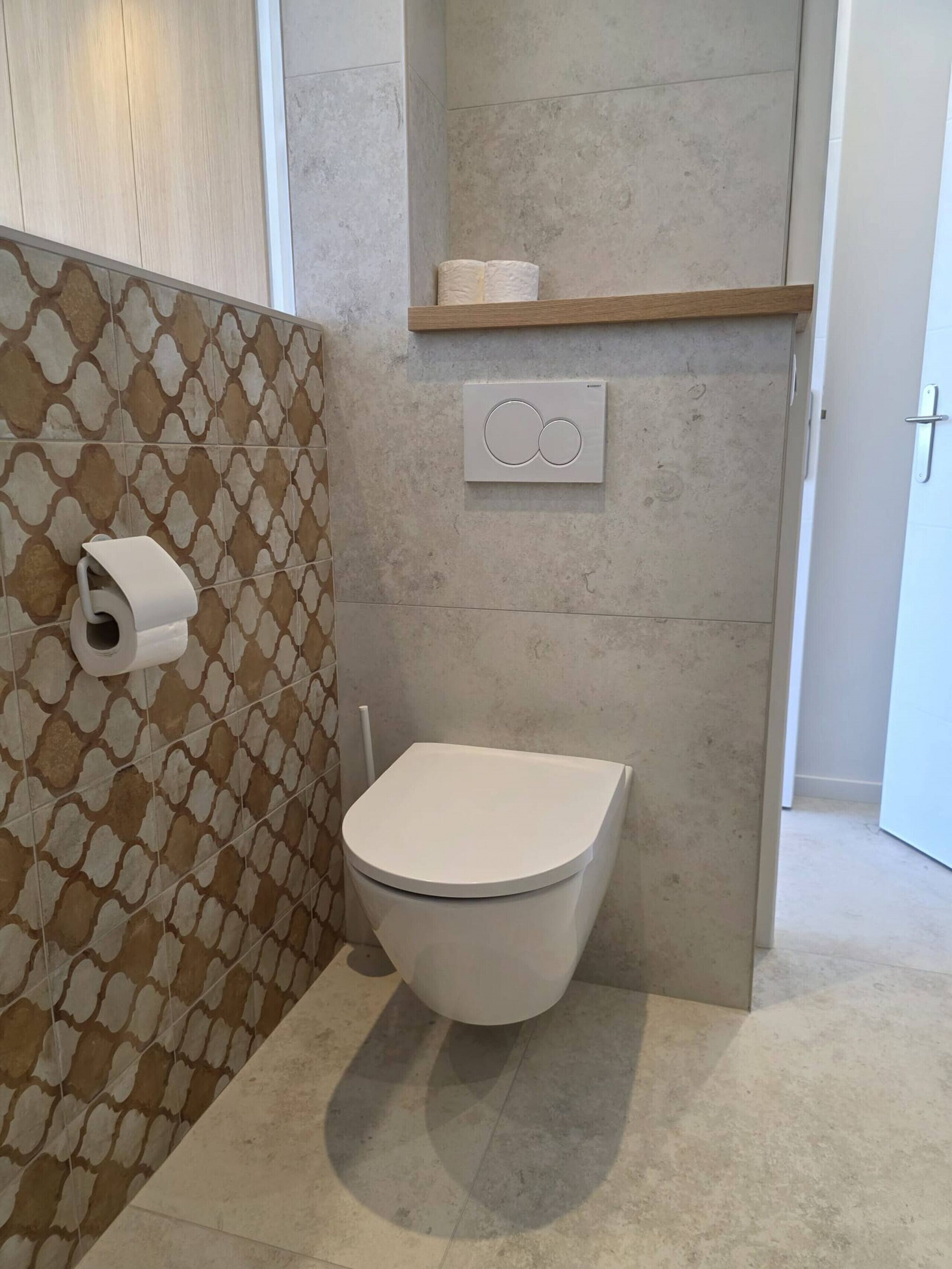 A bathroom with a patterned wall, a toilet, a paper towel dispenser, and a toilet paper holder.