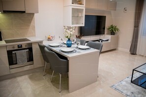 Een moderne keuken met een ingebouwde oven, een eethoek met een centraal kookeiland, en een aan de muur bevestigde televisie.
