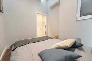 Ein Schlafzimmer mit einem Bett, Kissen, einem Fenster und einer Tür zu einem Flur.