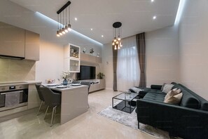Een moderne keuken met een centraal eiland, een eethoek met een zwarte bank en een woonkamer met een grote televisie.