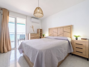 Ein Schlafzimmer mit einem Bett, einem Nachttisch aus Holz, einer Pendelleuchte, einer Topfpflanze und Blick durch eine Schiebetür.
