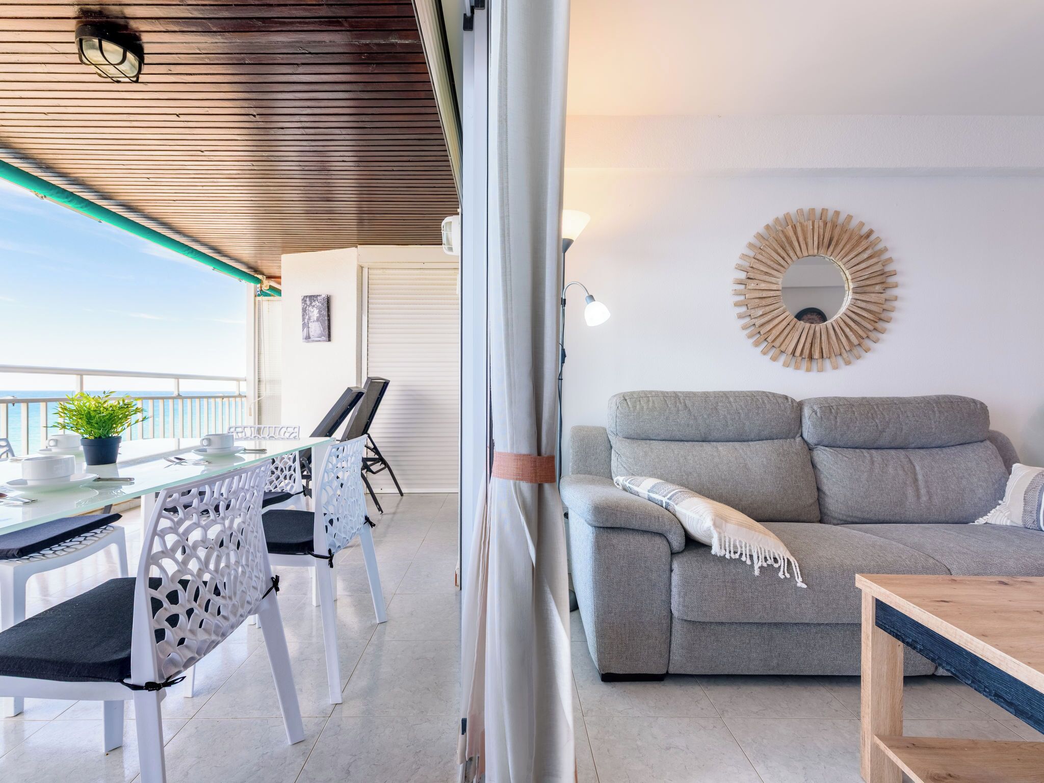 Een balkon met een tafel, stoelen, een bank en een decoratieve spiegel.