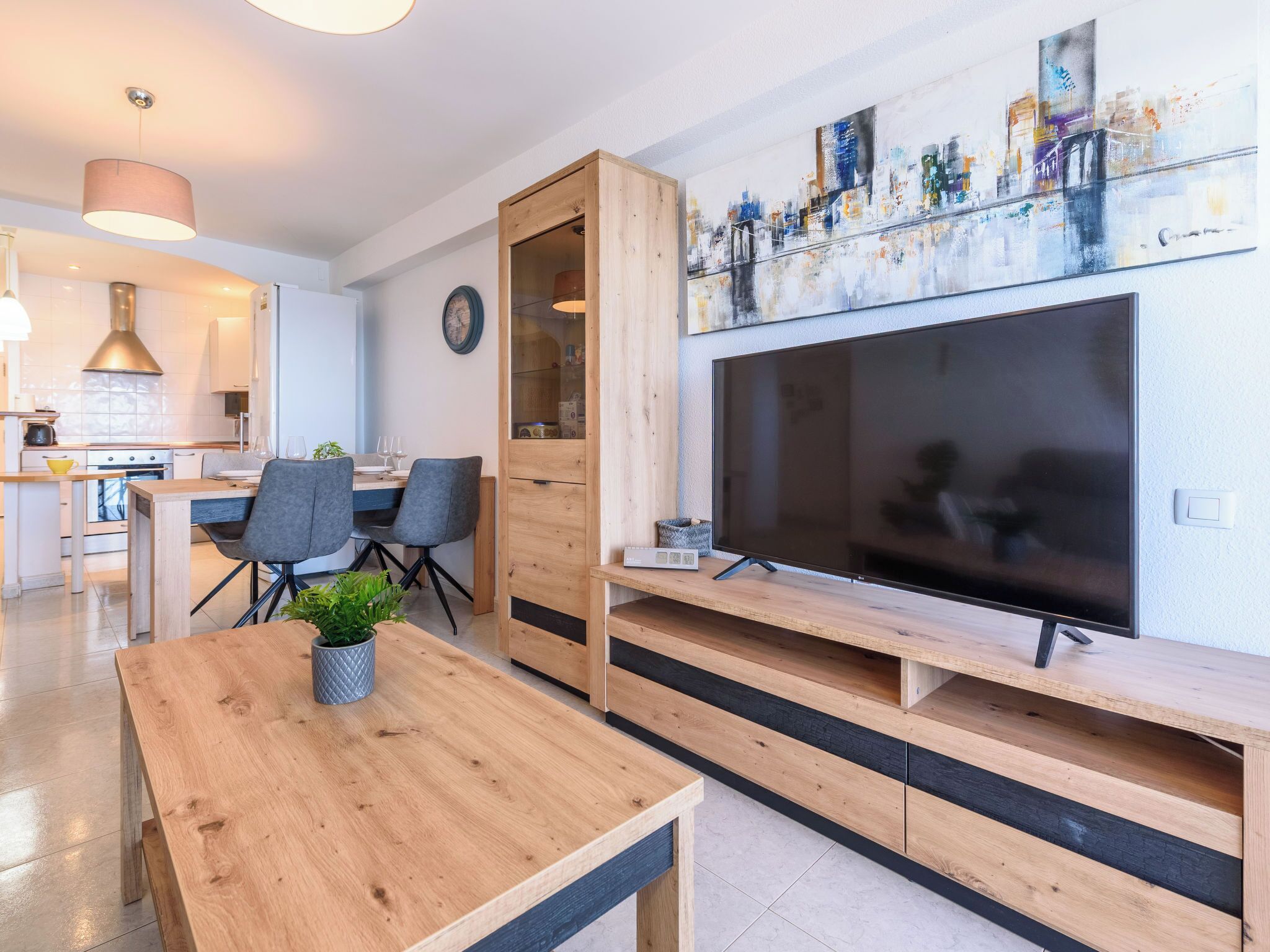 Een moderne woonkamer met een houten eettafel, een televisie op een houten meubel en een keuken op de achtergrond.