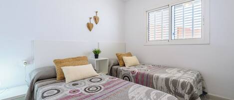 Un dormitorio con dos camas, una mesita de noche con una planta, aire acondicionado instalado en la pared y una ventana con persianas.