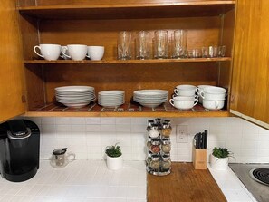 Eine Küche mit Kaffeemaschine, Regalen mit Tassen und Tellern sowie einer Gewürzleiste.