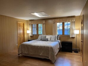 Ein Schlafzimmer mit einem Bett, Nachttischen, einem Fenster mit Vorhängen und einer Deckenleuchte.