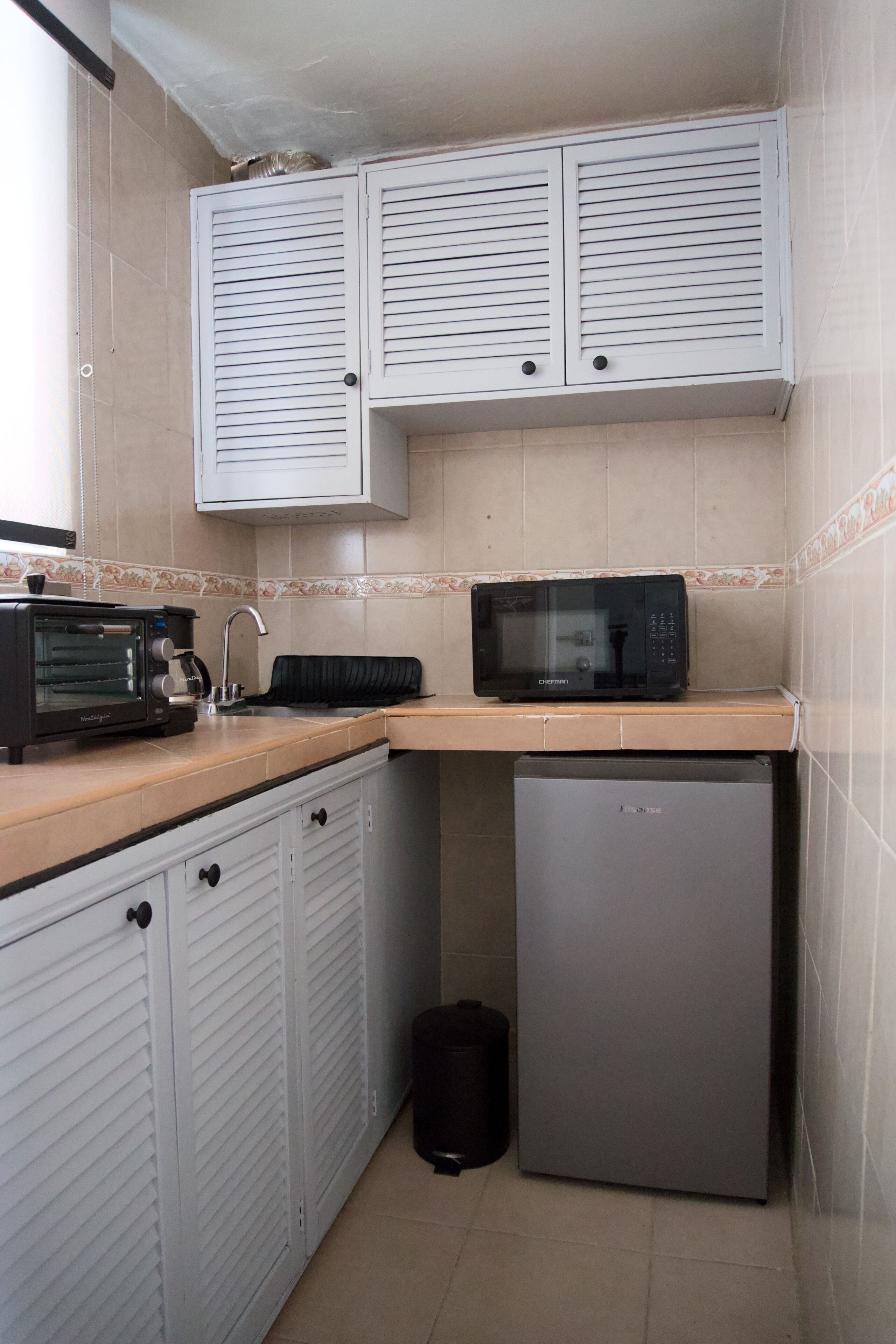 A compact kitchen with white cabinets, a microwave, a toaster, and a small refrigerator.