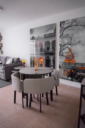 Een moderne woonkamer met een ronde tafel en stoelen, een bank en een groot stadsgezichtschilderij aan de muur.