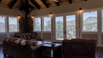 Un salon chaleureux avec un mur en pierre, un plafond en bois et de grandes fenêtres donnant sur les collines.