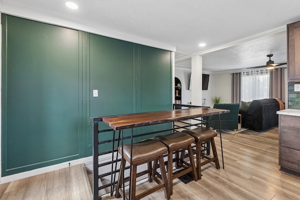 Eine moderne Küche mit einer Holztresen und Barhocker, ein Essbereich mit Tisch und Stühlen und eine Wand in Grüntönen.