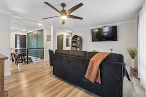 Ein Wohnzimmer mit einer Couch, einem Deckenventilator, einem Flachbildfernseher und einer Treppe, die zu einer weiteren Ebene führt.