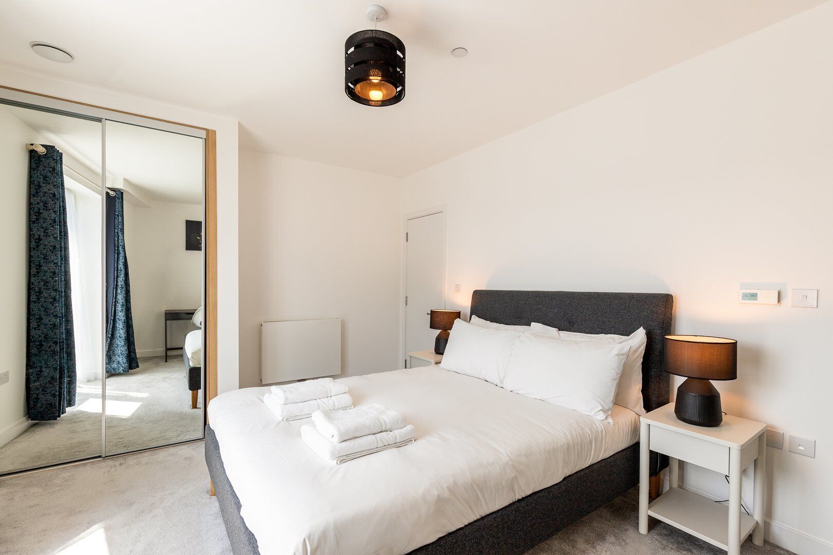 Quarto moderno com uma cama grande, luminárias de cabeceira, um espelho e um radiador.