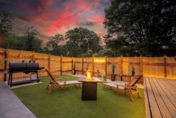 Ein Garten mit Grill, Feuerstelle und Holzliegen.