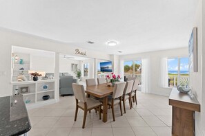 Un vaste espace dédié à la salle à manger, avec une table et des chaises en bois, un plafond blanc et une vue sur la plage.
