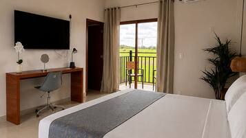 Habitación de hotel con una cama grande, un escritorio con silla, televisor y balcón con vistas.