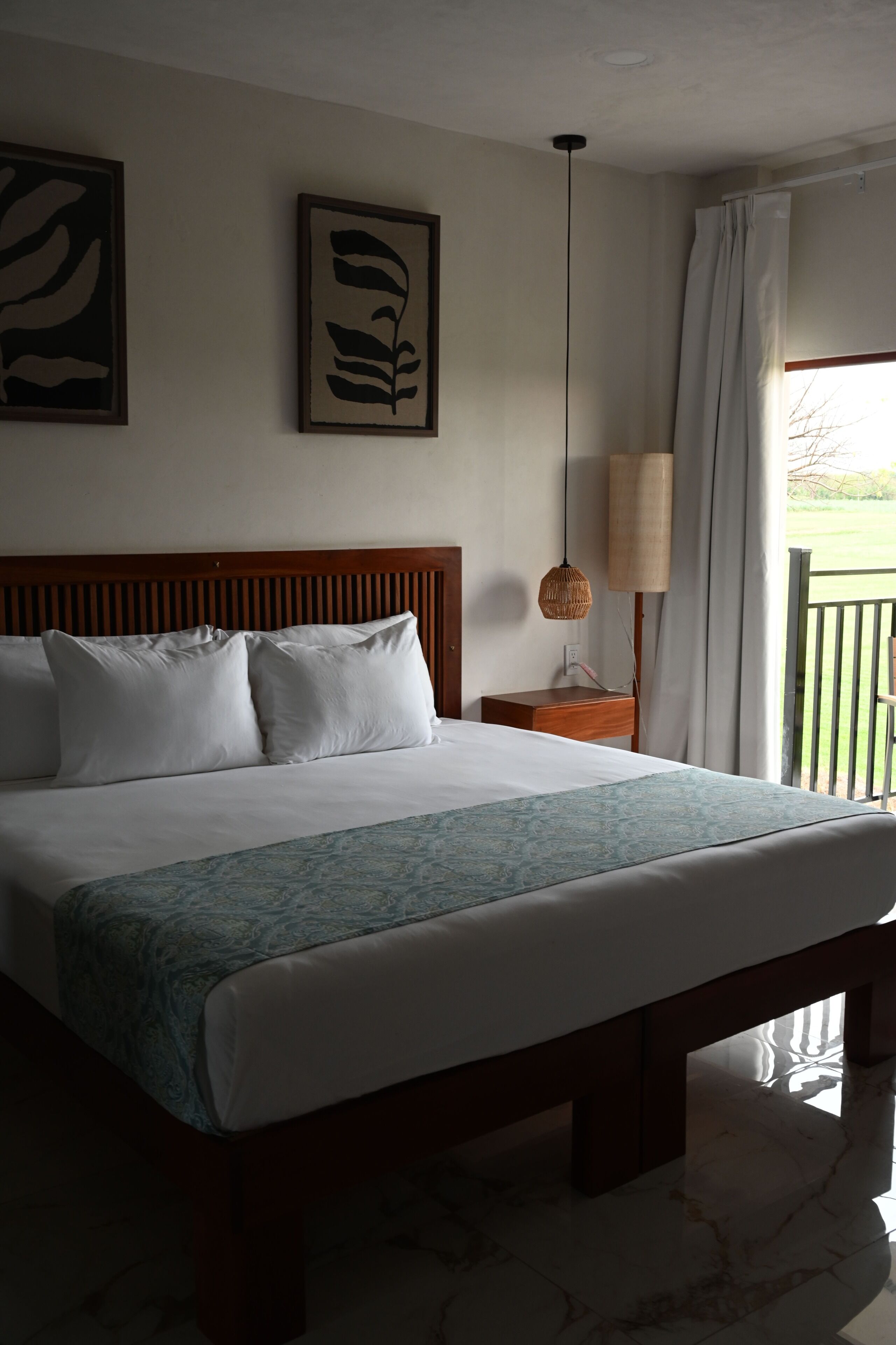 A hotel room with a large bed, a wooden headboard, a bedside table with a lamp, and two framed artworks on the wall.