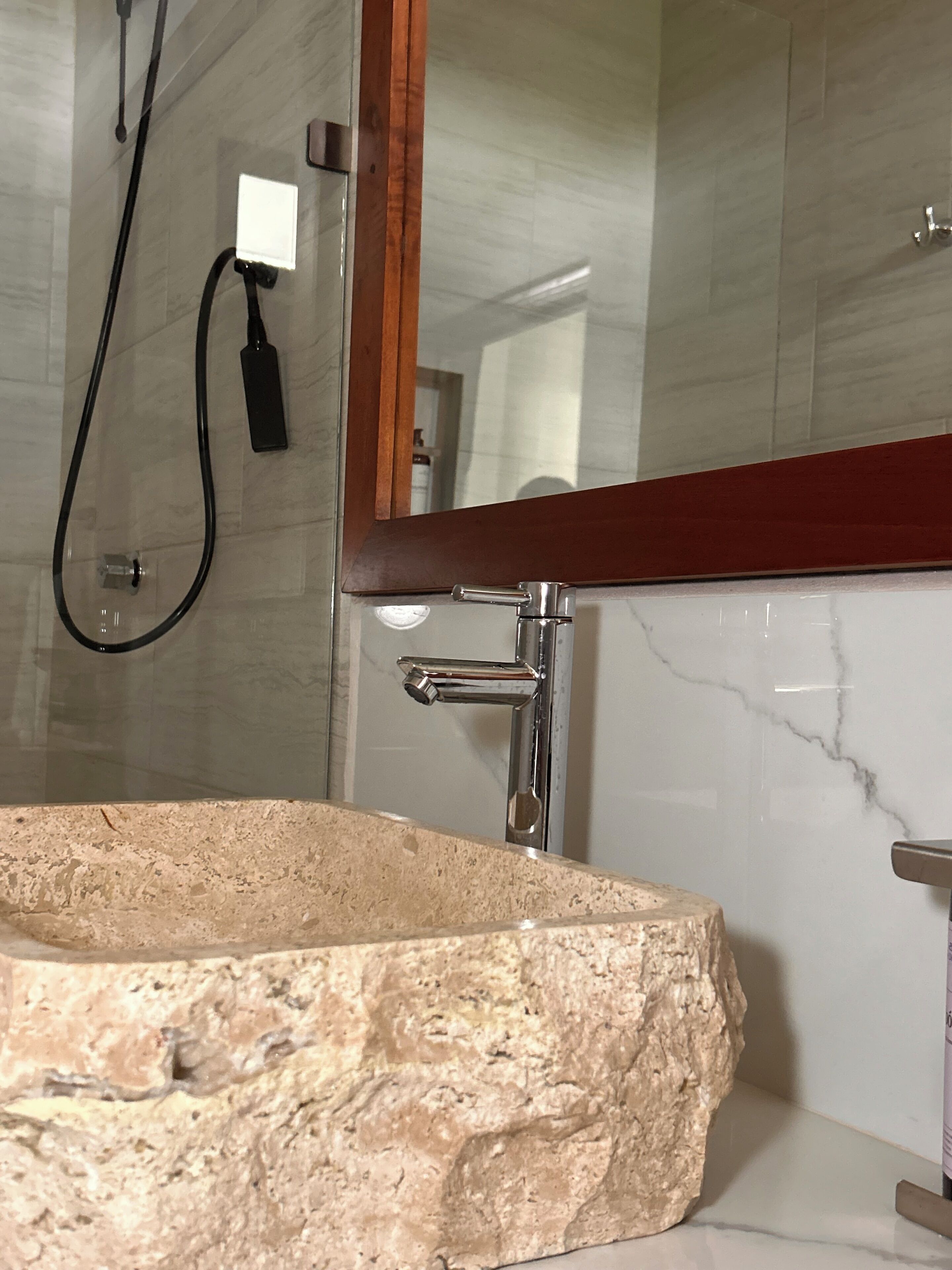 Un baño con lavamanos de piedra, un espejo y zona de ducha.