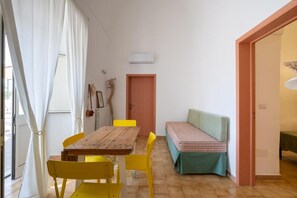Ein Zimmer mit einem Holztisch, gelben Stühlen, einer Bank mit grüner Auflage und einer weißen Klimaanlage sowie einer Tür mit rosa Rahmen.