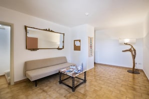 Una habitación con un sofá, una mesa con revistas, un espejo, un tablón de anuncios y una lámpara de pie.