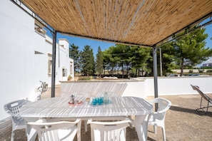 A covered outdoor dining area with a table and chairs, a pergola overhead, and a view of trees and buildings in the background. - Apartment 'A Casa Di Legnointesta' with Private Terrace, Wi-Fi and Air Conditioning (Nardò)