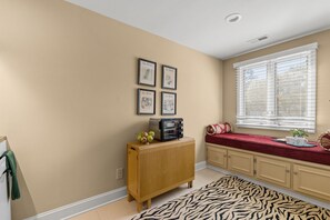 Ein Zimmer mit einem Holzkasten, einem mit Jalousien versehenen Fenster, einem zebra-gemusterten Teppich und gerahmten Bildern an der Wand.