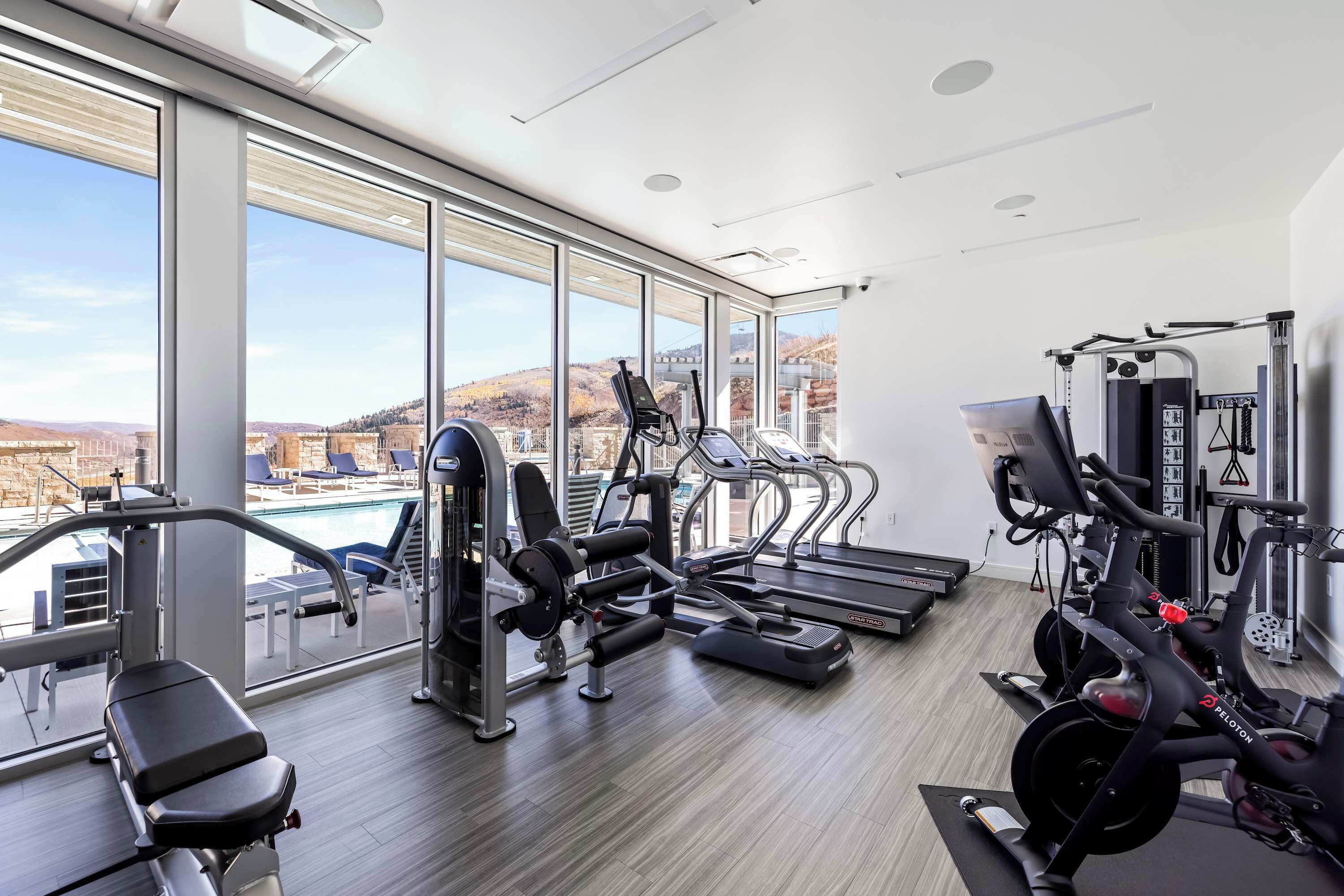 A gym with cardio machines, weight equipment, and a view of a pool and mountains.