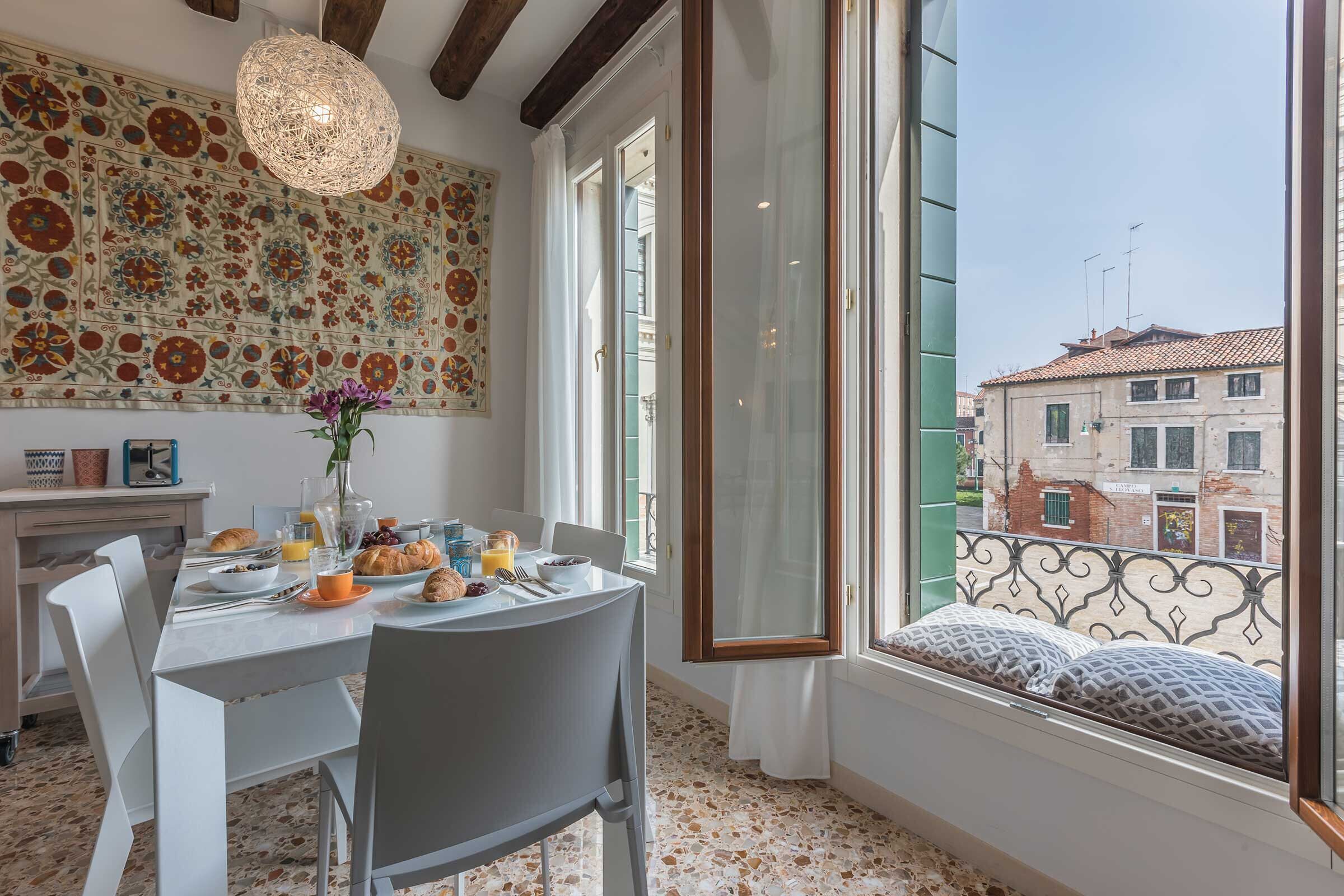 Un comedor con una mesa dispuesta para el desayuno, una pared decorativa y vistas de la ciudad a través de una ventana.