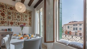 Ein Essbereich mit einem für das Frühstück gedecktem Tisch, einer Wand mit Dekoration und Blick auf die Stadt durch ein Fenster.