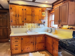 Une cuisine avec des meubles de rangement en bois, un évier, une cuisinière et une fenêtre.