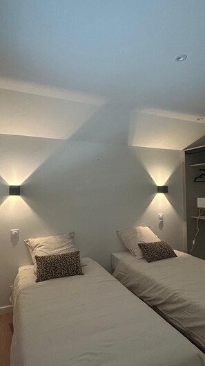 A bedroom with two beds, each with a pillow, and two wall-mounted lights.