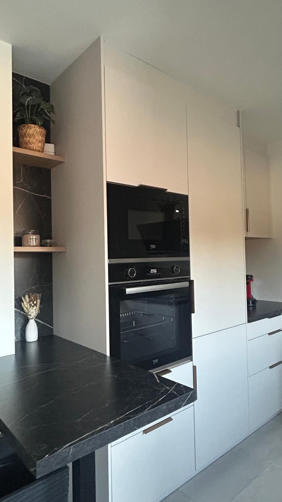 Een moderne keuken met een ingebouwde oven en magnetron, witte kastjes en een marmeren aanrecht.