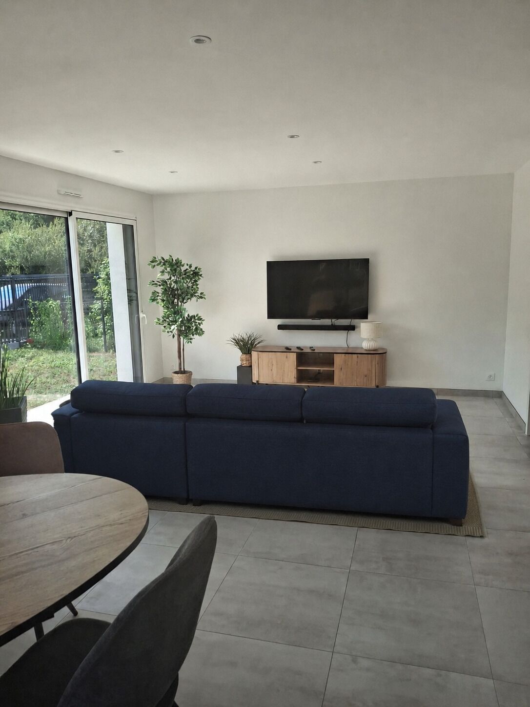 A modern living room with a large TV, a blue sofa, a dining table, and a potted plant.