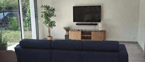 A modern living room with a large TV, a blue sofa, a dining table, and a potted plant.