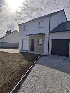 Une maison moderne à deux étages, dotée d’un garage, d’un petit porche à l’avant et d’une pelouse bien entretenue.