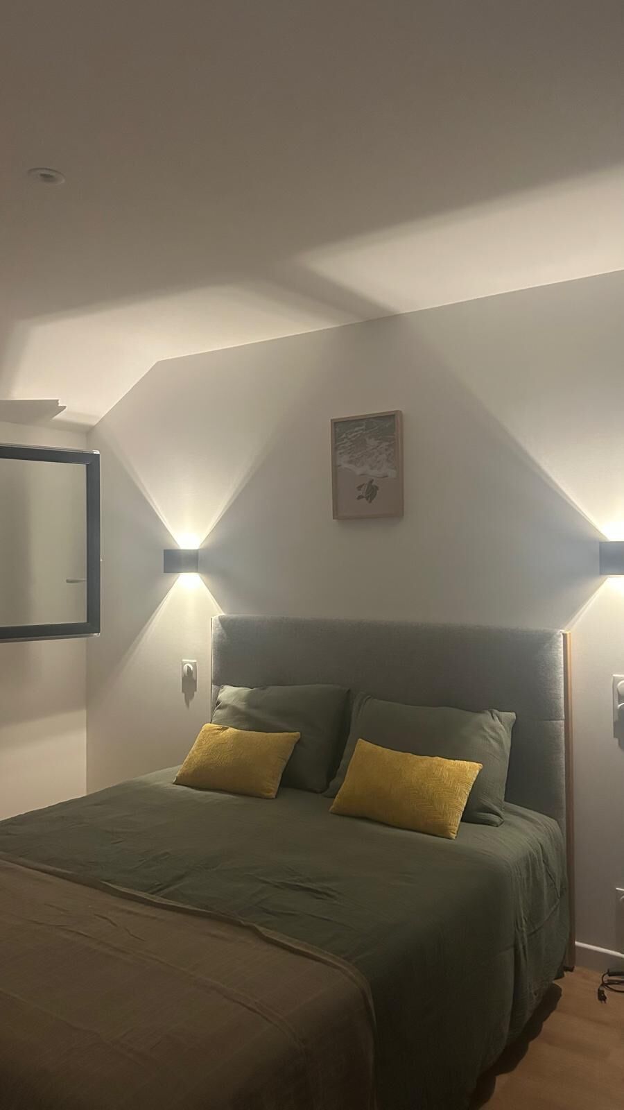 A bedroom with a bed, two bedside lamps, a wall-mounted artwork, and a door.