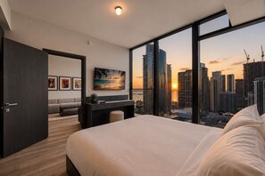 A modern bedroom with a large bed, a desk, and a view of a cityscape at sunset. - Luxury E11EVEN 1BR Skyline Views & ELITE Amenities (Miami)