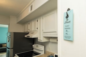 Eine Küche mit weißen Schränken, einem Herd und einer Mikrowelle. Ein Schild an der Wand weist auf Gastparkplätze mit einer Wohneinheitnummer hin.