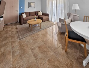 Ein Wohnzimmer mit braunem Sofa, einem runden Holztisch, einem weißen Esstisch und einer Lampe.