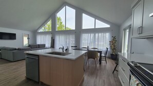 A modern kitchen with a central island, a dining area with a table and chairs, a sofa, and a TV mounted on the wall.