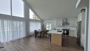 A modern kitchen with a central island, wooden flooring, and large windows.