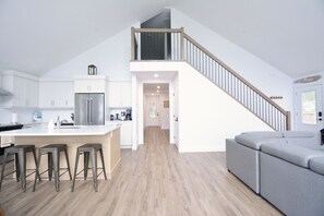 Eine moderne Küche mit einer zentralen Kochinsel, Barhocker, einer Treppe und einem grauen Sofa.