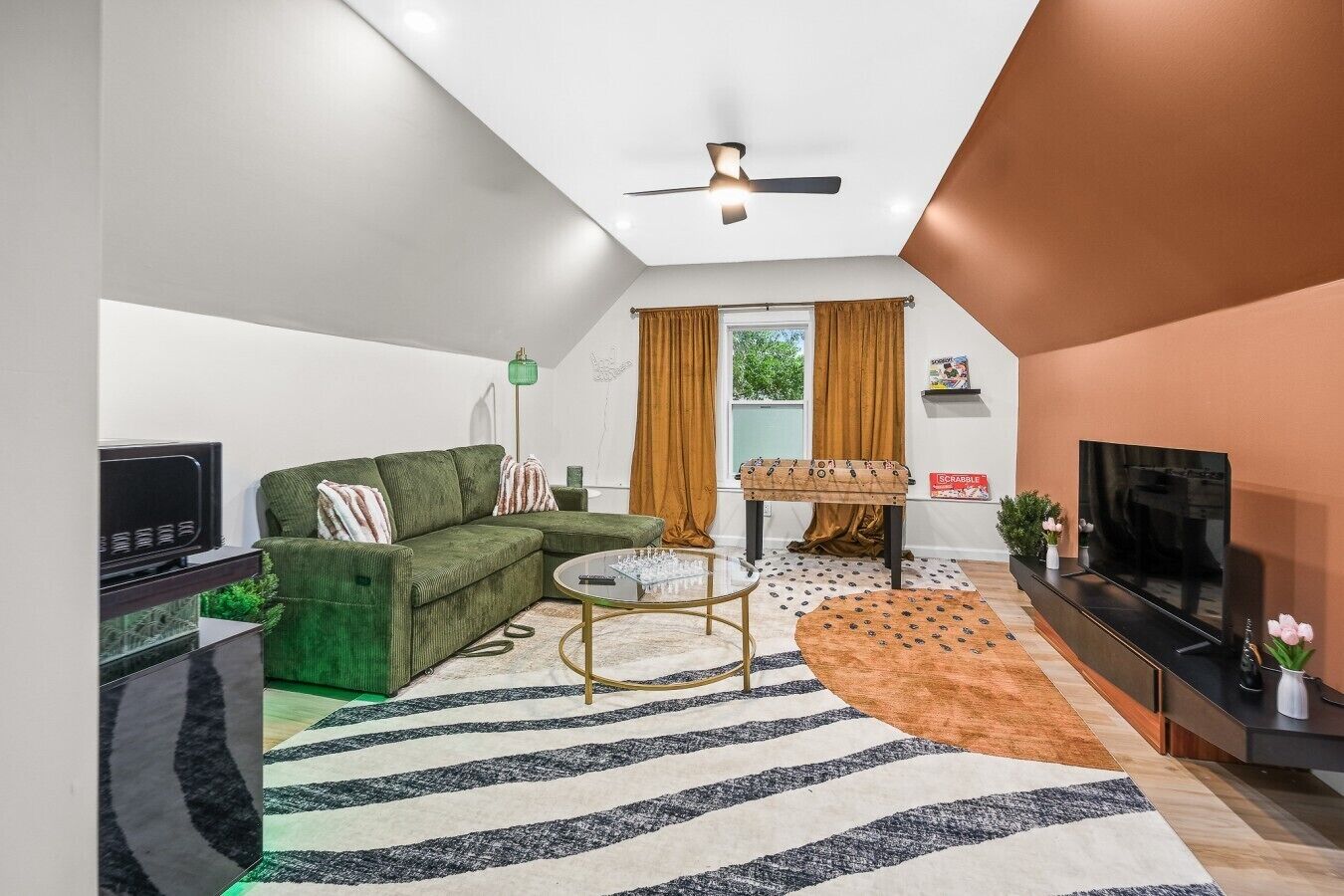 Een moderne woonkamer met een hoekbank, een salontafel, een flatscreen televisie en een plafondventilator.