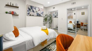 Moderni hotellihuone, jossa on sänky, työpöytä, tuoli, kattotuuletin ja suuri ikkuna.