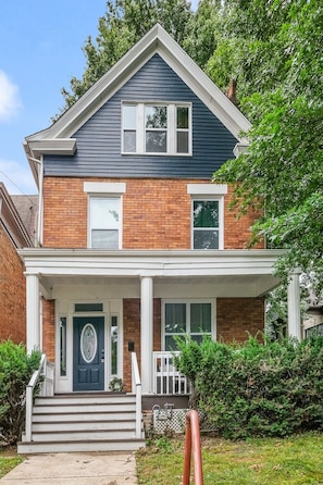 A two-story house with a front porch, a brick facade, and a dark blue roof.