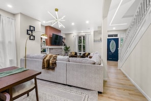 A modern living room with a sofa, a dining table, and a staircase leading to a door.